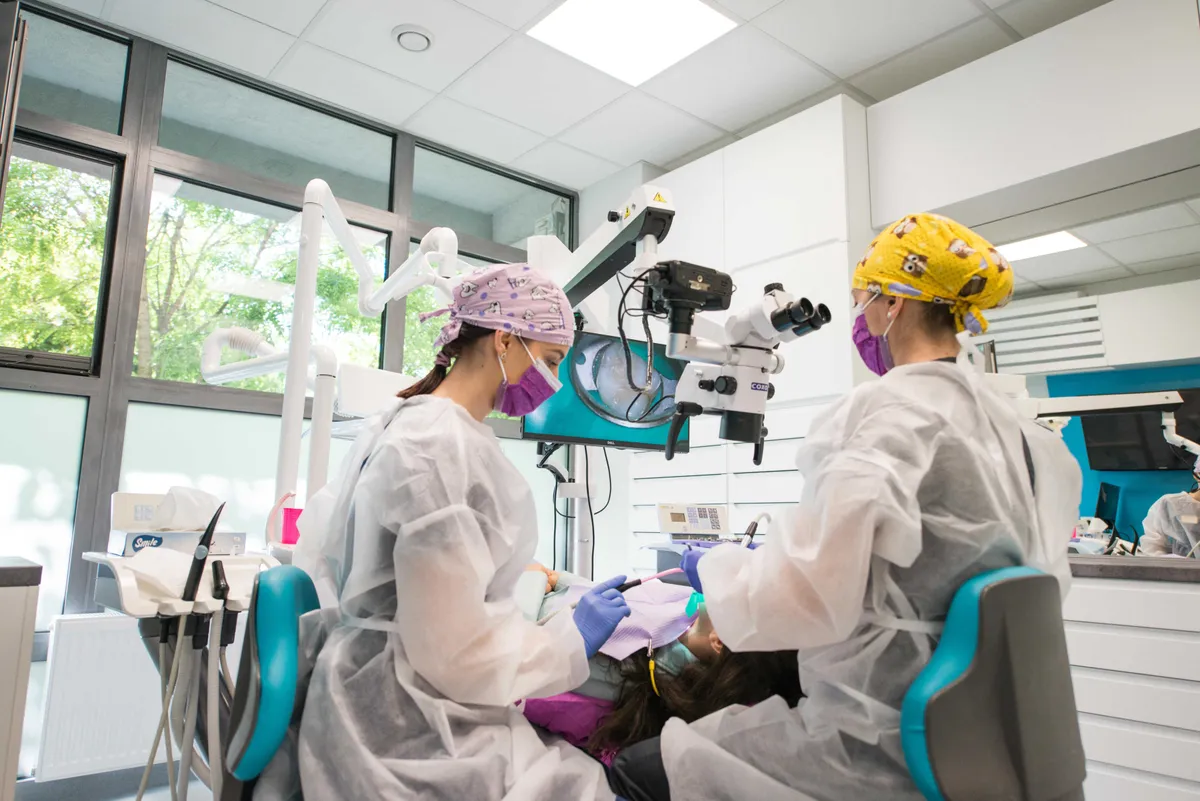 Doi medici Olidental Clinic tratează o pacientă cu ajutorul microscopului dentar